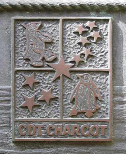 Photo montrant une plaque métallique sur laquelle un rectangle divisé en plusieurs segments est gravé. Un ourse, un manchot, la Petite Ourse et la Croix du Sud sont représentés.